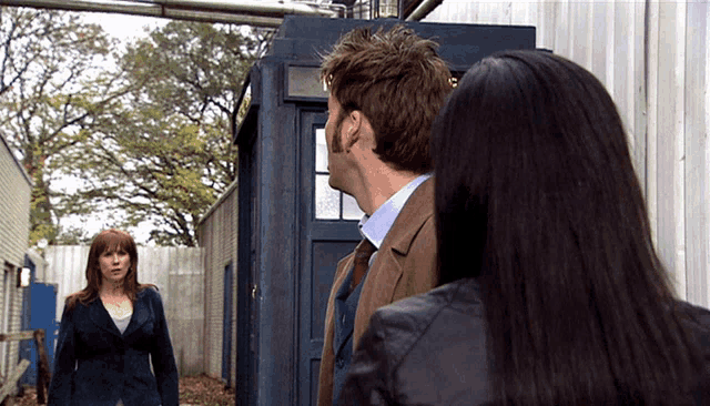 a man and two women are standing in front of a blue police box