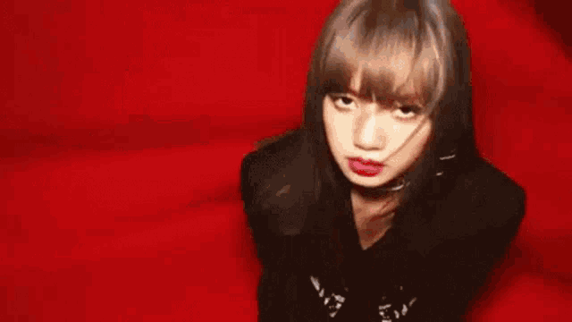 a woman wearing a black jacket and choker is standing in front of a red curtain .