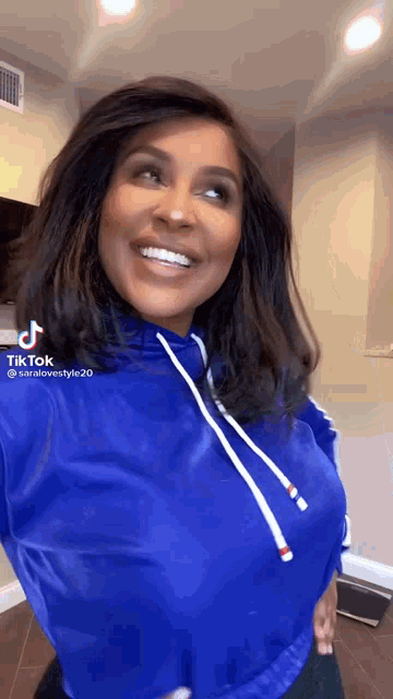 a woman wearing a blue hoodie is smiling and looking at the camera .