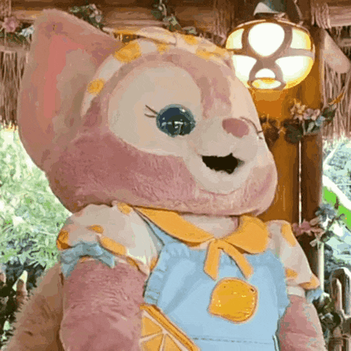 a stuffed animal wearing overalls and a yellow collar is standing next to a lamp .