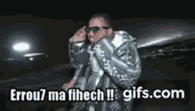 a man wearing sunglasses and a jacket is standing in front of a plane and says gifs.com on the bottom .