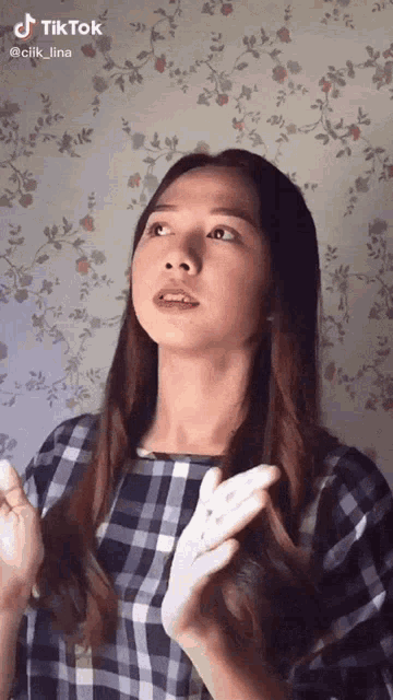 a woman in a plaid shirt is holding a white object in her hands and has a tiktok sticker on her face