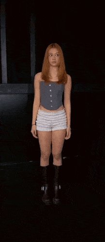 a woman is dancing in a dark room wearing shorts and boots .