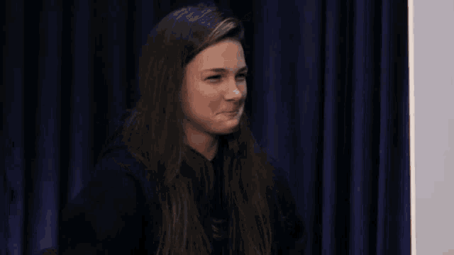 a woman sitting in front of a blue curtain