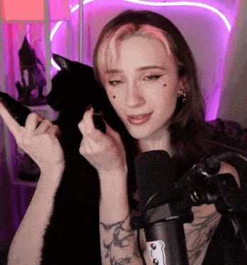 a woman with pink hair is holding a black cat in front of a microphone that says seiko