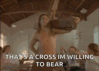 a man without a shirt is holding a cross in a room with people .