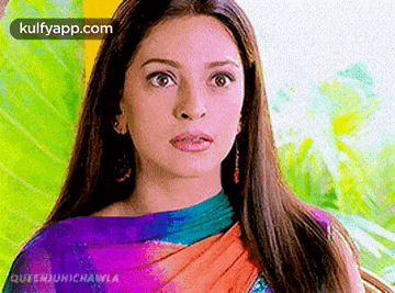a woman in a colorful saree is making a funny face while standing in front of a colorful background .