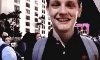 a young man with a backpack is smiling in front of a building