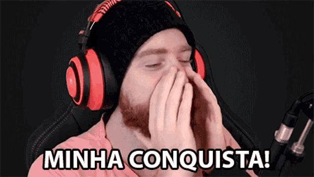 a man wearing headphones and a beanie is covering his mouth with his hands and the words minha conquista are above him