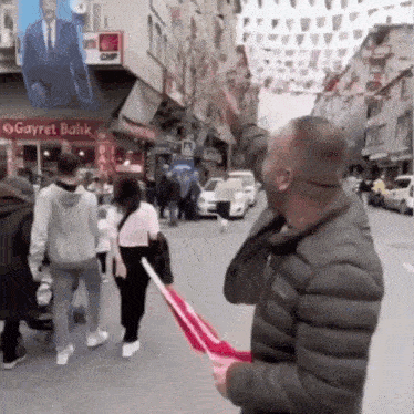a man is walking down a street holding a flag in front of a sign that says gayret balik