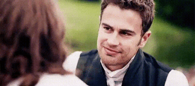 a man in a vest and tie is looking at a woman in a white shirt .