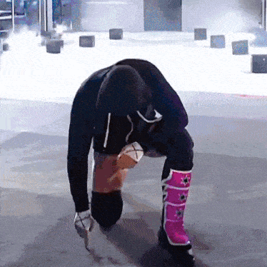 a person wearing a black hoodie and pink boots kneeling down