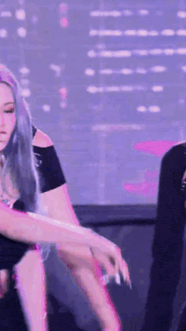 a woman with purple hair is dancing on a stage in front of a purple background