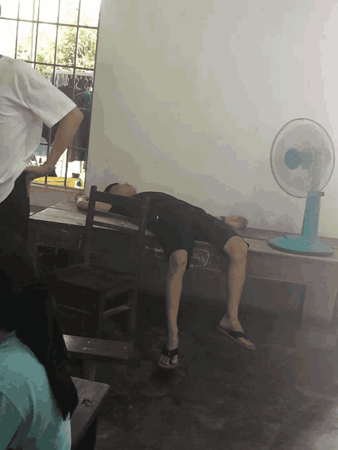 a man is sleeping on a chair with a fan in the background