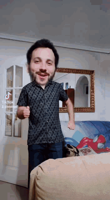 a man in a black shirt is dancing in a living room with a spider man statue in the background