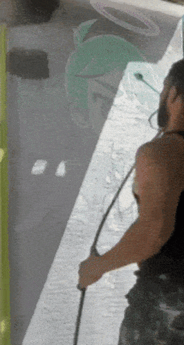 a man with a beard is holding a hose in front of a sign that says ' t ' on it