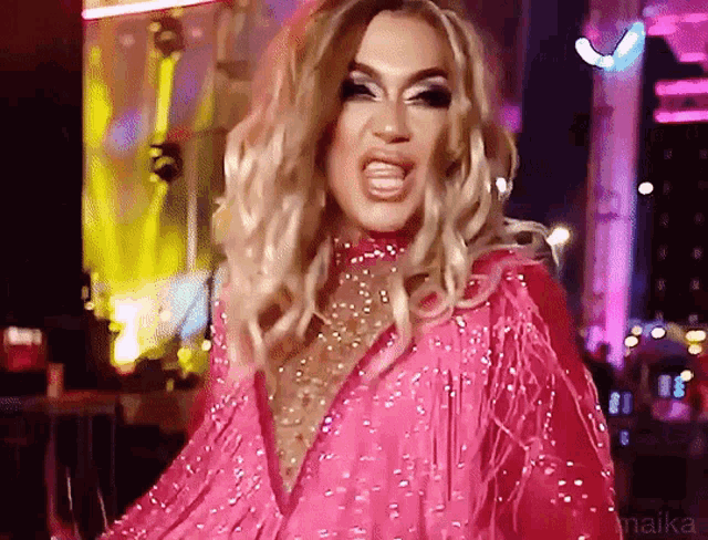 a drag queen is wearing a pink dress with fringe