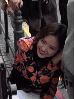 a woman in a floral shirt smiles while sitting on a bench