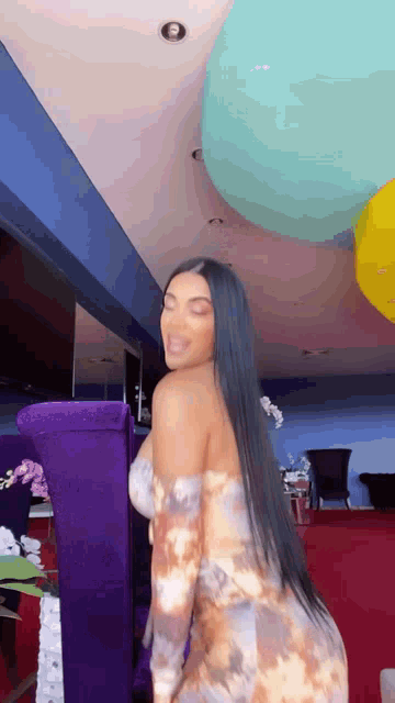 a woman in a tie dye dress is dancing in a room with balloons hanging from the ceiling .