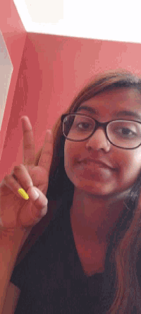 a girl wearing glasses is holding a yellow object in her hand and giving a peace sign