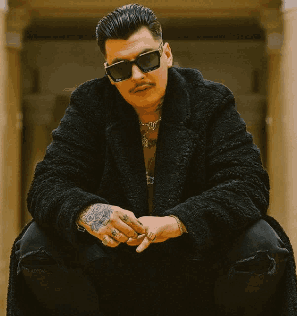 a man wearing sunglasses and a black coat has a tattoo on his wrist