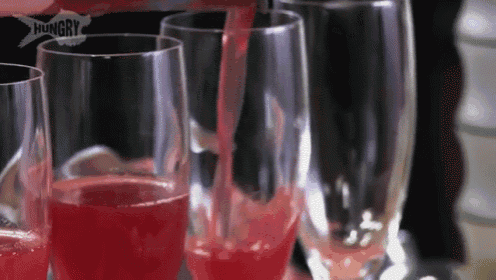 a person is pouring red liquid into a glass with the word hungry on the bottom .