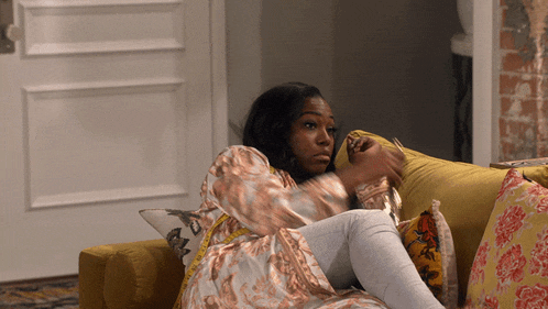 a woman is laying on a yellow couch with a pillow that says r on it