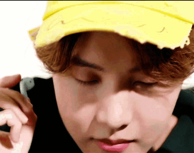a close up of a man wearing a yellow hat talking on a cell phone