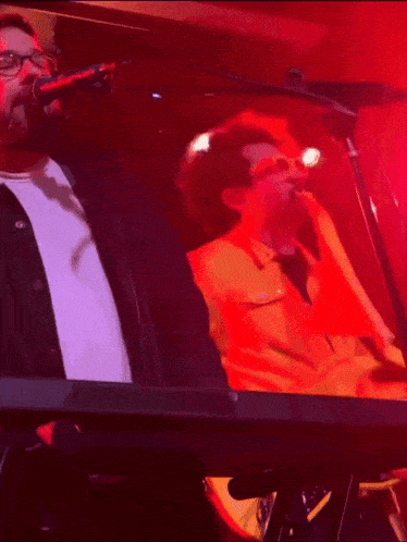 a man singing into a microphone while playing a keyboard with a yellow shirt that says ' nsfw '