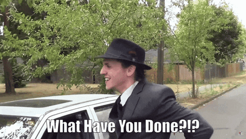 a man in a suit and hat is standing in front of a car with the words " what have you done " on the bottom