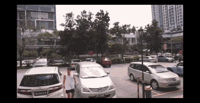 a man is walking in a parking lot with cars parked and one of them has a license plate that says b4 9058 b