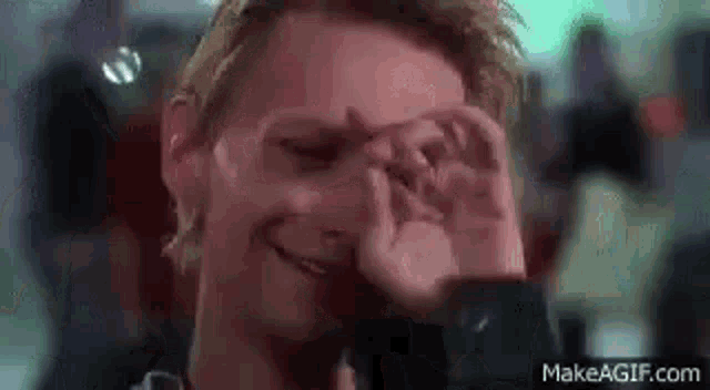 a man is covering his eyes with his hands in a close up of a movie scene .