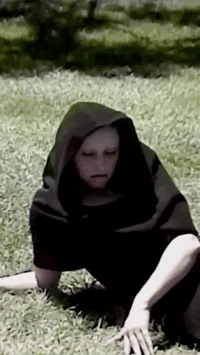 a person wearing a black hooded cape is crawling through the grass