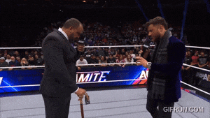 a man in a suit is talking to another man in a wrestling ring with a sign that says mite on it