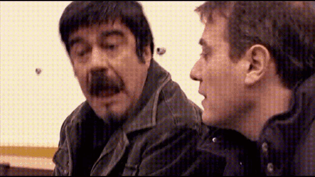 a man with a beard and mustache talks to another man