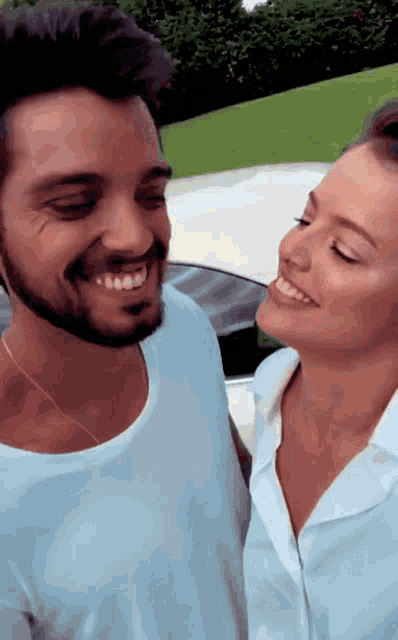 a man and a woman are smiling and looking at each other in front of a car