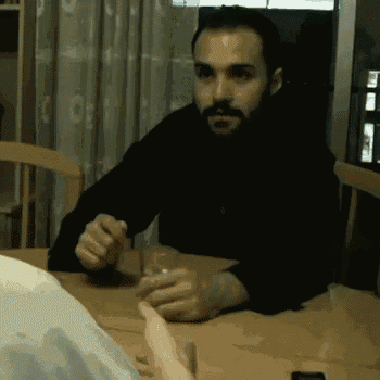 a man with a beard is sitting at a table with a glass of water .