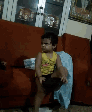 a little boy is sitting on a red couch with a newspaper in front of him that says ' weekly ' on it