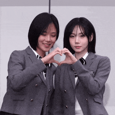 two girls in school uniforms making a heart with their hands