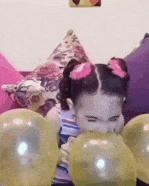 a little girl blowing up balloons on a couch .