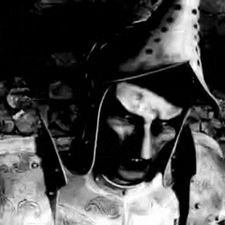 a black and white photo of a man wearing a knight 's armor and a hat .