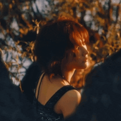 a woman in a black dress is standing in a forest