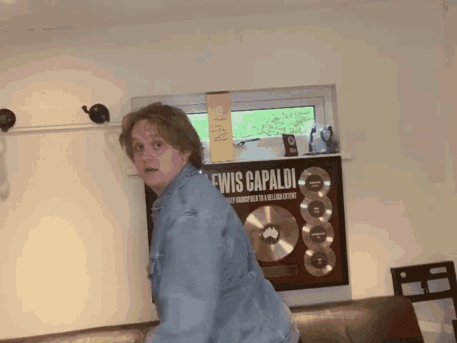 a man in a denim jacket is standing in front of a poster for lewis capaldi