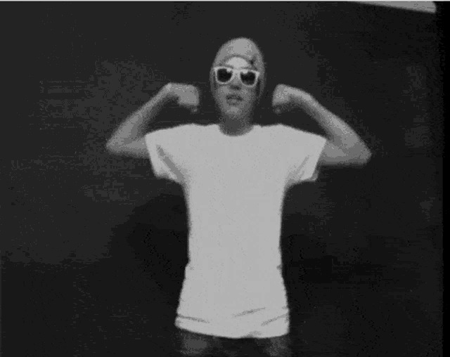 a man wearing sunglasses and a beanie flexes his muscles