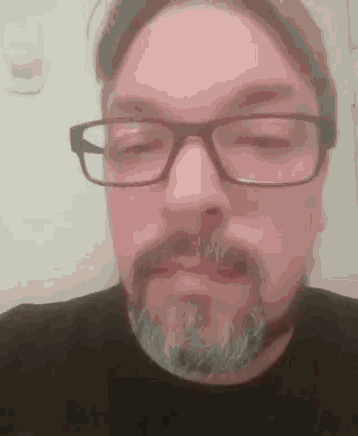 a man with glasses and a beard is wearing a black shirt .