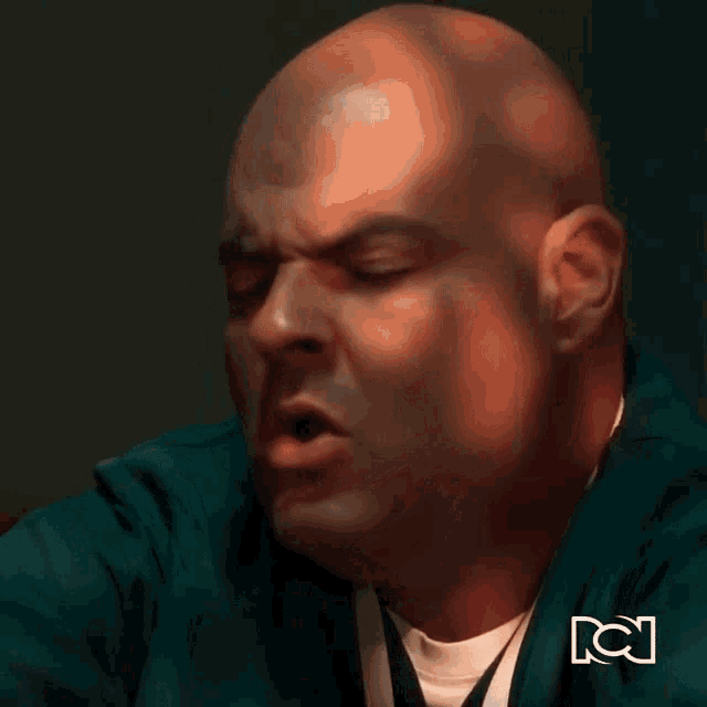 a bald man in a green jacket is making a funny face in front of a tv channel logo