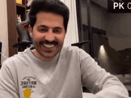 a man with a mustache is smiling while wearing a gray sweatshirt .