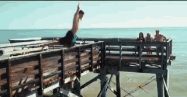 a man jumps off a wooden pier into the ocean