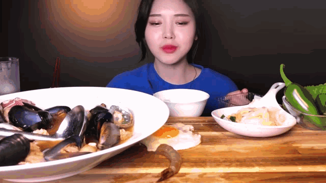 a woman in a blue shirt is eating a large bowl of seafood