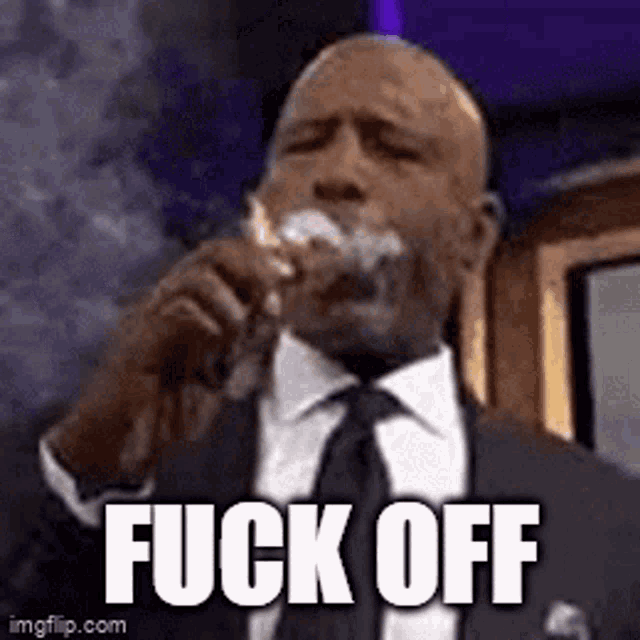 a man in a suit and tie is drinking from a glass with the words fuck off written on it .